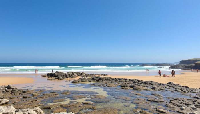 A sunny beach showcasing clear waves, golden sands ideal for sunbathing, rocky outcrops for exploration, accessible ramps, and diverse groups of people enjoying the sunny day.