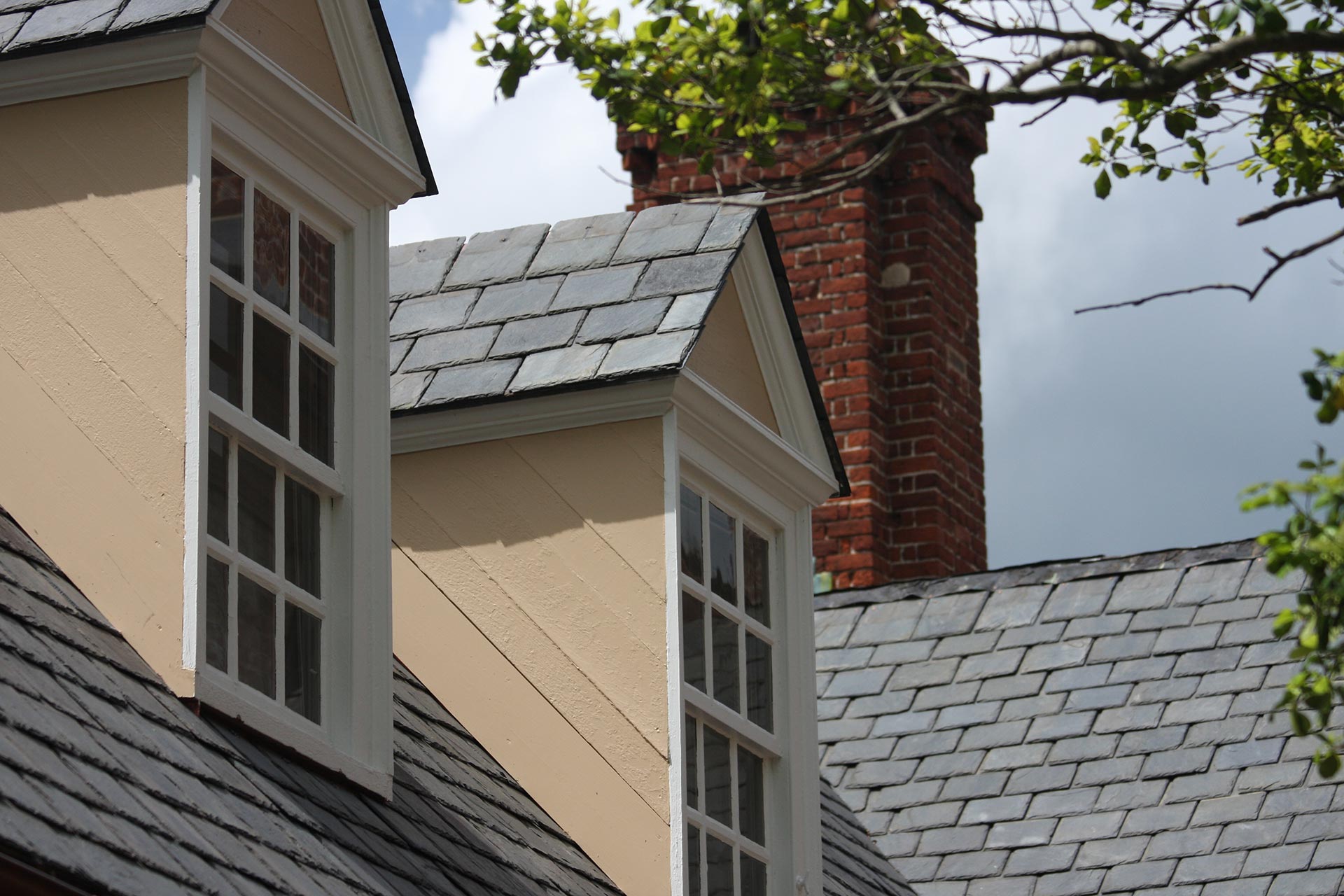 Traditional slate roof featuring two dormer windows and a brick chimney on a classic home